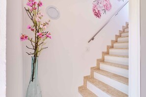 A staircase with a handrail, a vase with pink flowers, and a wall-mounted light fixture. - Holiday apartment with two bedrooms in a quiet location (Nerezine)