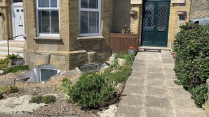 Een stenen gebouw met een groene deur, huisnummer 8, en een kleine tuin met een pad naar de ingang.
