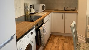 Een kleine keuken met witte kastjes, een magnetron, een waterkoker en een wasmachine.