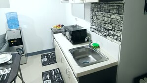 Et lille køkken med hvide skabe, en sort mikroovn, en vask og en vanddispenser.