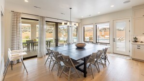 A spacious dining area with a large table, multiple chairs, and a central light fixture. - Sleeps 25, Private Pool, Hot Tub & Courts, Playground (St. George)