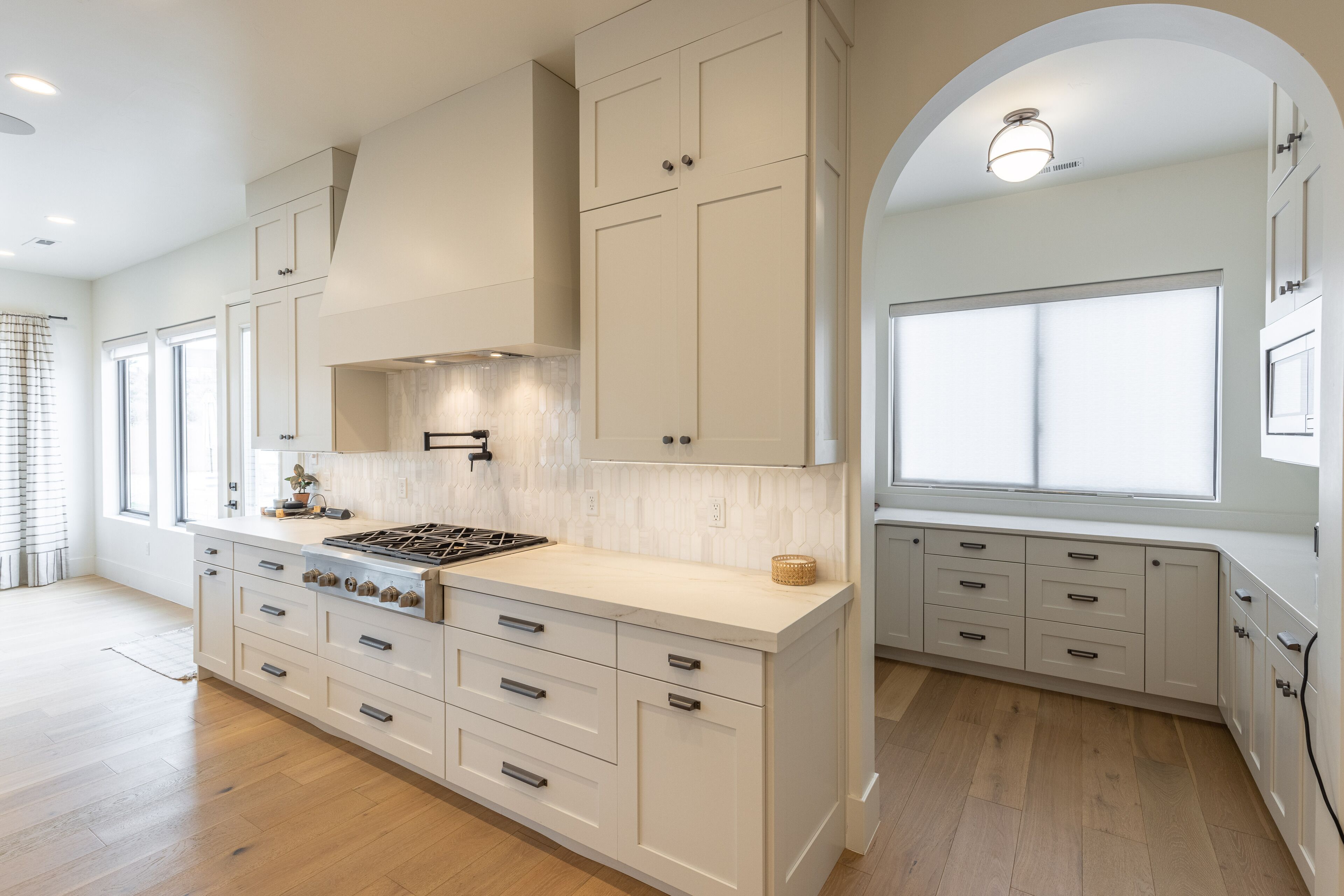 Una cocina moderna con armarios blancos, una isla central con estufa y un amplio ventanal que proporciona luz natural.