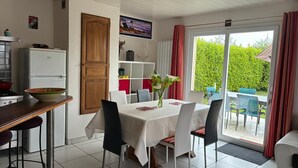 A dining area with a table set for four, a kitchen with a refrigerator, and a sliding glass door leading to an outdoor seating area. - Audierne/Plouhinec: 1 km from the sea, in a peaceful, enclosed setting. (Plouhinec)
