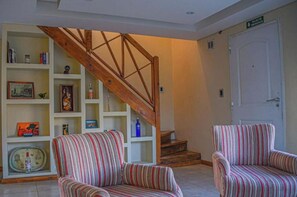 A living room with striped armchairs, a wooden staircase, and a bookshelf with various items.