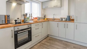 A modern kitchen with white cabinets, a wooden countertop, a built-in oven, and a stainless steel range hood.