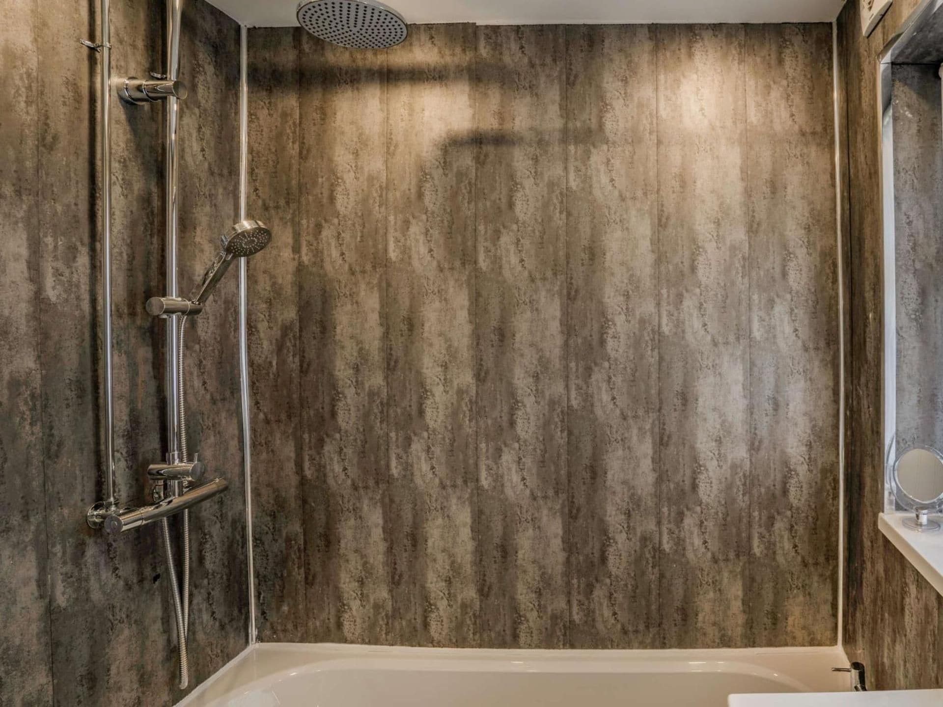 Un baño con bañera, ducha con múltiples cabezales y espejo instalado en la pared.