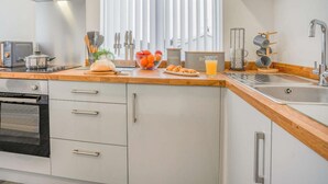 A modern kitchen with a stainless steel range hood, a built-in oven, a double sink, and a window with blinds.