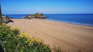 A beach with a rocky outcrop and a building on top.