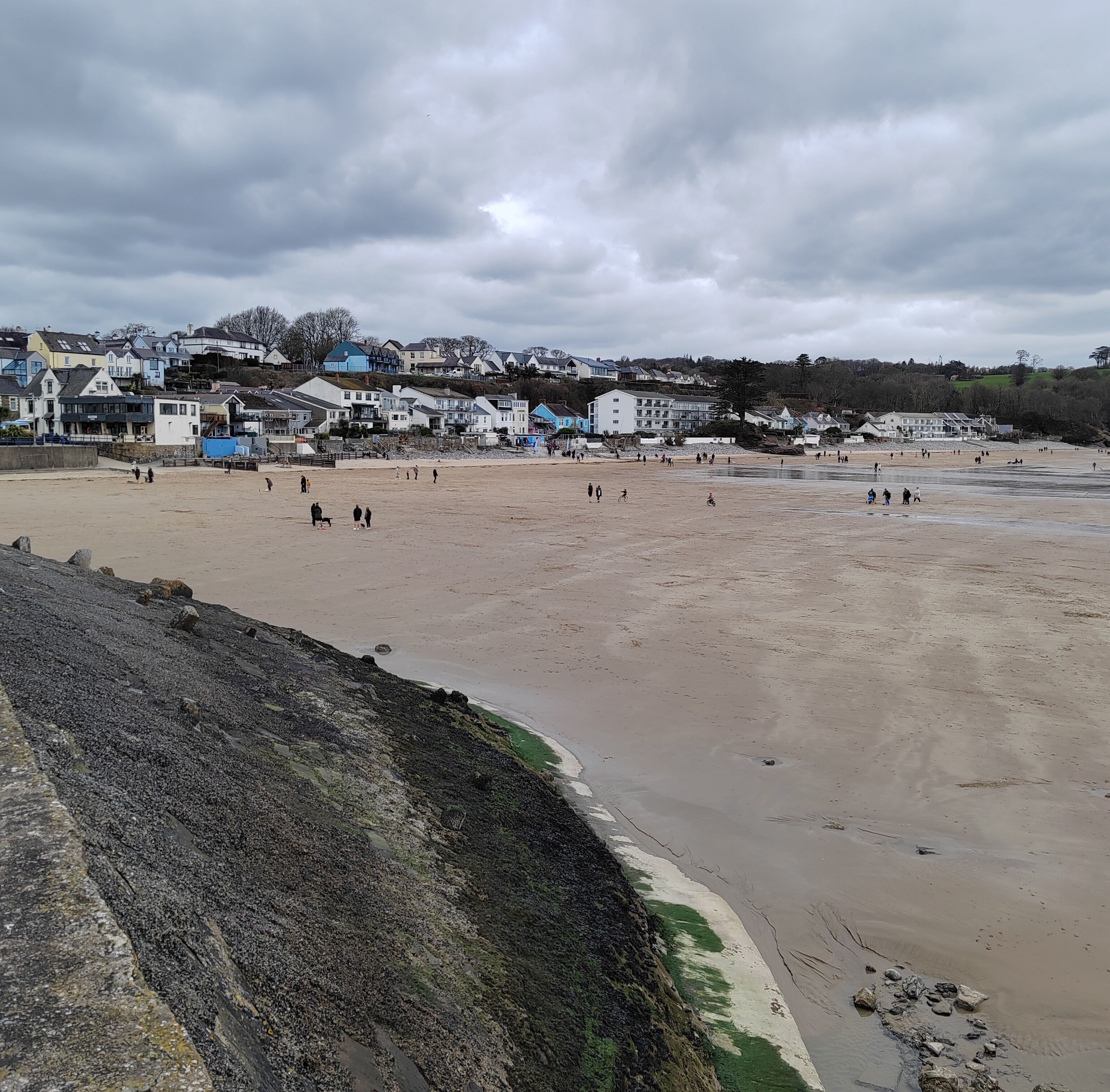 A beach with houses in the background and a rocky shoreline.