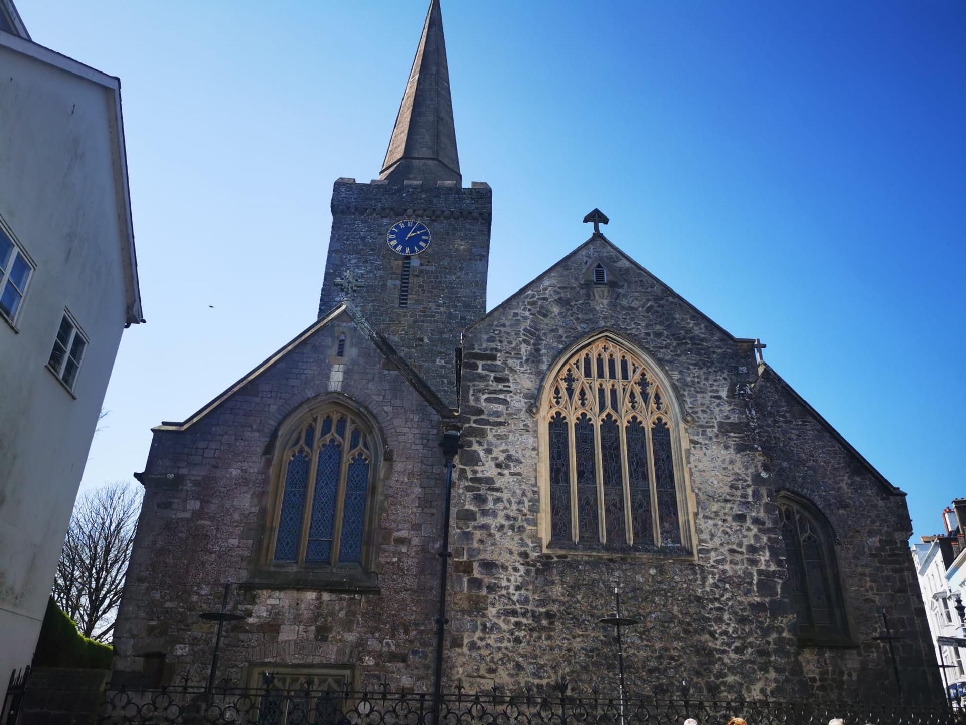 A church with a tall steeple, a clock, and large arched windows.