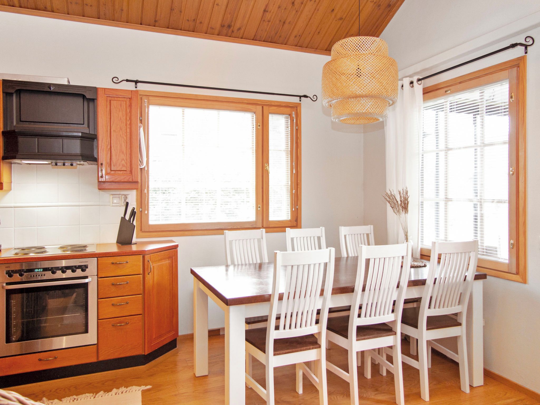 A kitchen with wooden cabinets, a stove, and a dining table with white chairs.