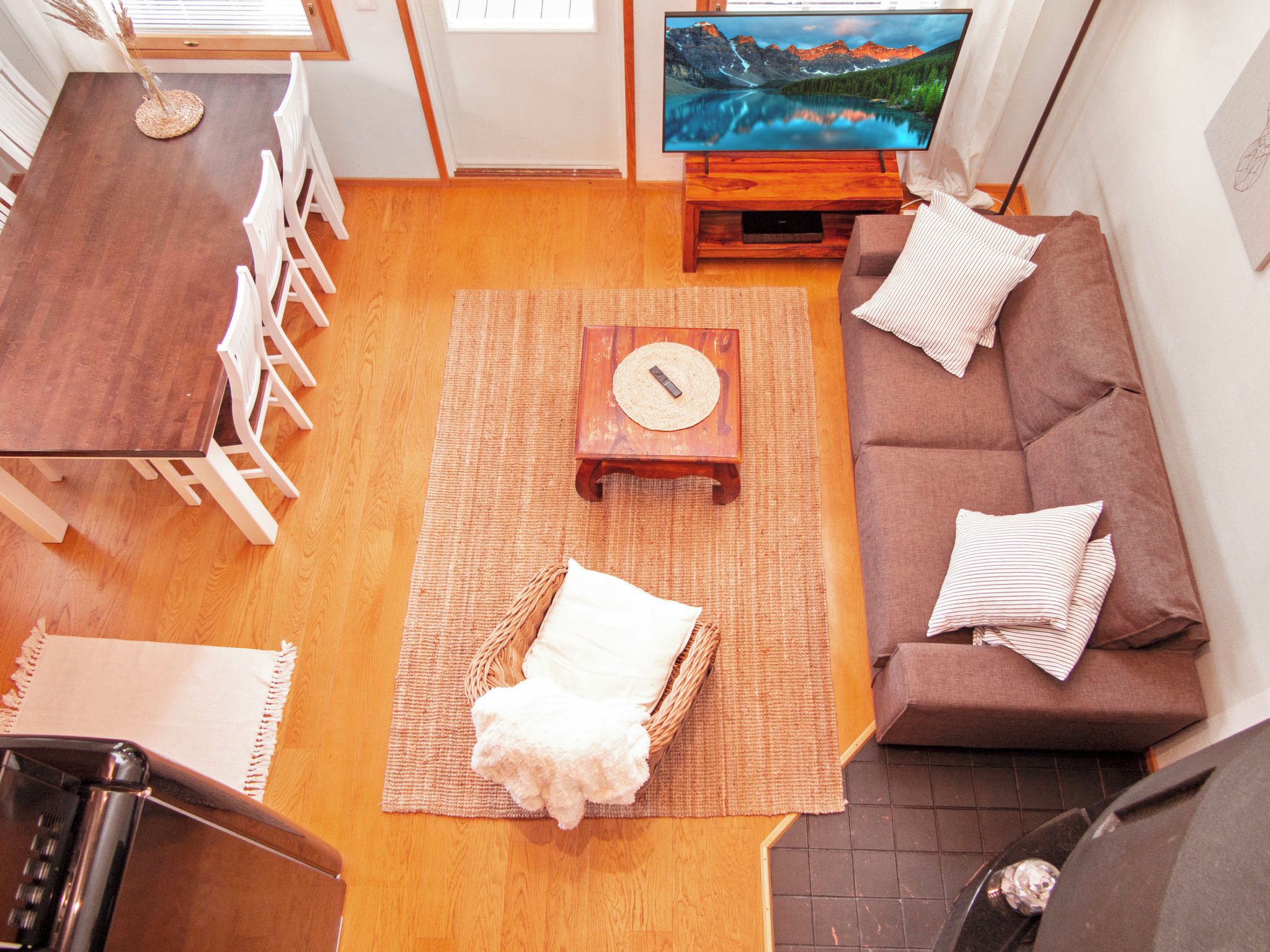 A living room with a wooden dining table, white chairs, a brown sofa, a television, and a small wooden coffee table.