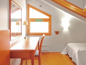 Una habitación pequeña y acogedora con una mesa y sillas de madera, una ventana con vistas y una cama con sábana blanca.