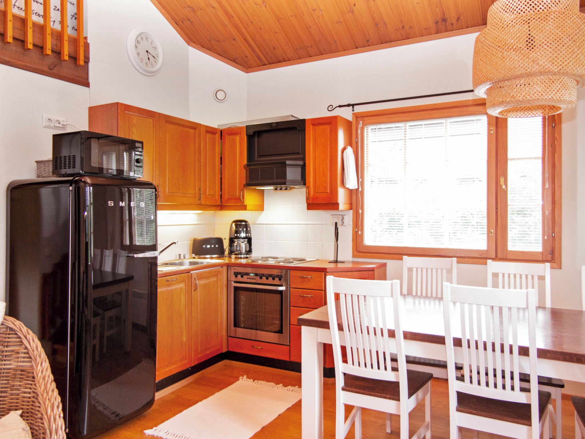 Une cuisine avec des meubles de rangement en bois, un réfrigérateur noir, une cuisinière et une table à manger avec des chaises.