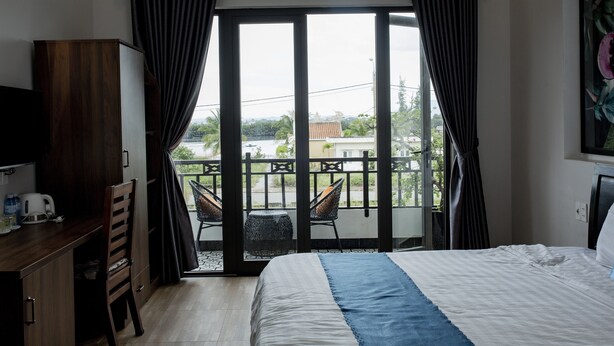 Ein Hotelzimmer mit Bett, Schreibtisch, Stuhl und einem Balkon mit Blick nach außen.