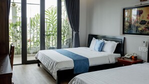 Ein Hotelzimmer mit zwei Betten, einem großen Fenster mit Vorhängen, einem Bild an der Wand und einem kleinen Tisch mit Telefon und Blumenvase.