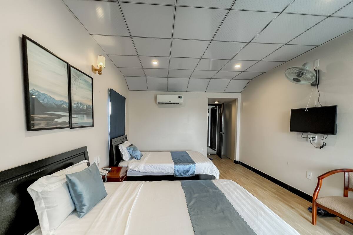 A hotel room with two beds, a TV, an air conditioning unit, and a painting on the wall.