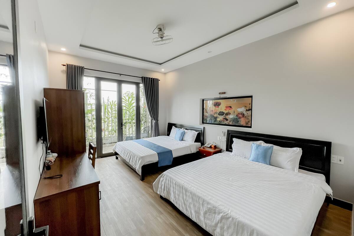 A hotel room with two beds, a desk, a TV, and a large window with curtains.