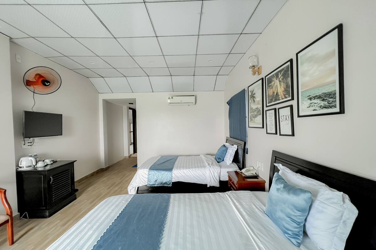 A hotel room with two beds, a TV, a desk with a phone, and artwork on the walls.