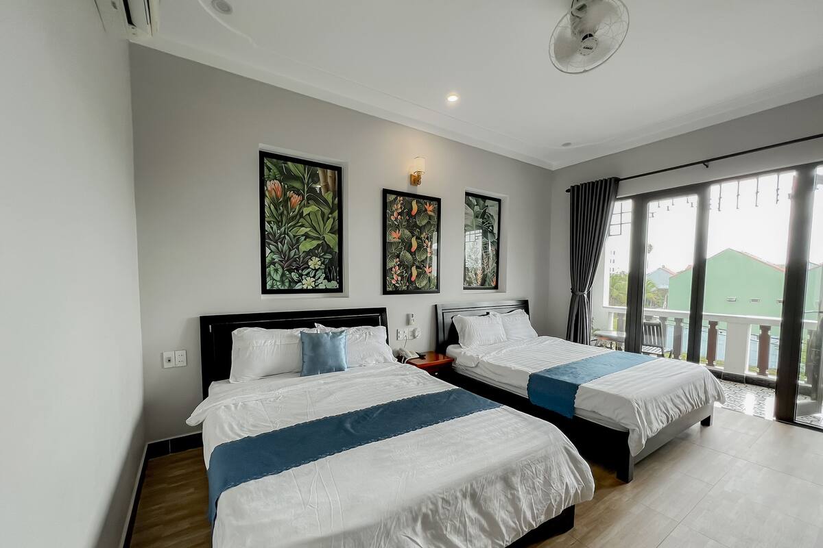 A hotel room with two beds, a large window with a view, and artwork on the wall.