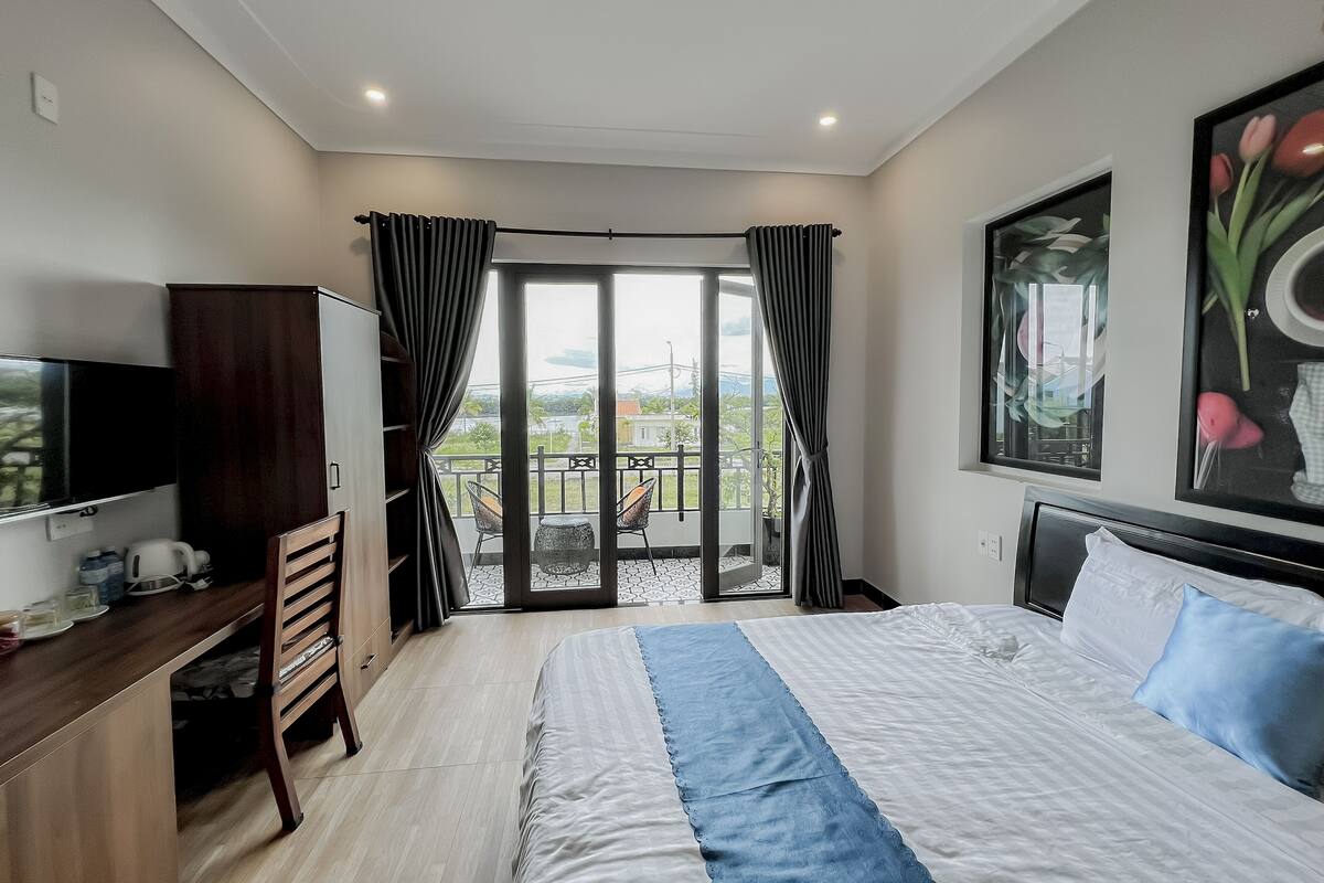 A bedroom with a bed, a desk, a TV, and a balcony with a view.