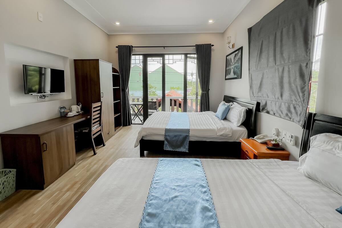 A hotel room with two beds, a TV, a desk, and a balcony with a view.
