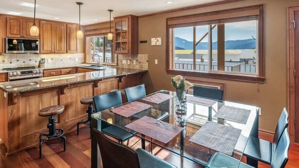 Una cucina moderna con mobili in legno, una grande isola centrale e un'area pranzo con tavoli e sedie in vetro.