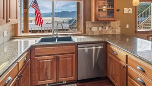 Una cucina con mobili in legno, lavastoviglie in acciaio inox, una finestra con bandiera americana e vista sulle montagne.