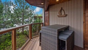 Un balcone con un tavolino e sedie in vimini, ringhiere in legno e vista su alberi ed edifici.
