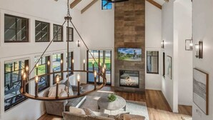 A spacious living room with a large chandelier, a fireplace, and a view of the outdoors through large windows. - Dover Bay Luxe Home w/ Private Hot Tub - Sleeps 12 (Dover)
