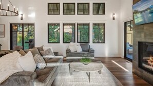 A modern living room with a fireplace, two sofas, a coffee table, and large windows. - Dover Bay Luxe Home w/ Private Hot Tub - Sleeps 12 (Dover)