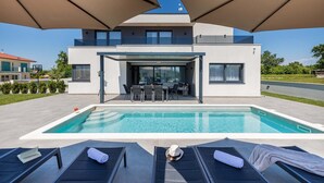 A modern poolside area with a pool, lounge chairs, and a covered outdoor dining area. - Villa Ana Skicini in Jursici (Jursici)