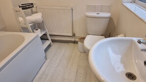 Une salle de bain équipée d’une baignoire, d’un lavabo, de toilettes et d’un radiateur.
