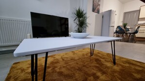 A modern living room with a white table, a large flat-screen TV, a potted plant, and a yellow rug. - Cosy Stay in Stoke on Trent By Villazu (Stoke-on-Trent)