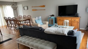 Ein Wohnzimmer mit einer Couch, einer Bank, einem Fernseher, Holzmöbeln und einem Essbereich mit Stühlen und einem Tisch.