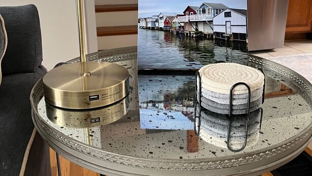 Ein runder Glastisch mit einer Metalllampe, einem Foto von Häusern auf dem Wasser und einem gewobenen Korb.