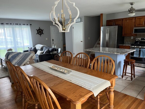 A dining area with a wooden table and chairs, a chandelier, and a kitchen in the background. - Canandaigua Lakeside Retreat (Canandaigua)