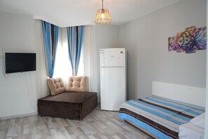 A bedroom with a bed, a sofa, a flat-screen TV, a refrigerator, and a window with curtains. - Taşev Suites (Bodrum)