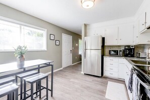 A modern kitchen with white cabinets, stainless steel appliances, and a dining area with a table and chairs. - Walking distance to USM_Heart of Hattiesburg! (Hattiesburg)
