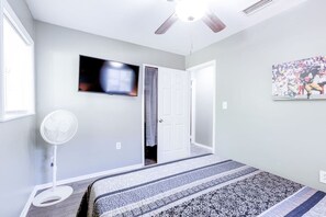 Een slaapkamer met een bed, een plafondventilator, een televisie en een deur naar een andere kamer.