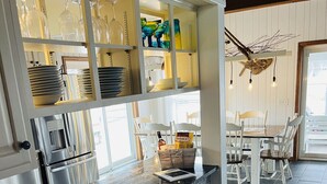 Une cuisine dotée d’un plan de travail en granit, de meubles blancs et d’un coin repas avec des chaises et une table, le tout dans des tons blancs.