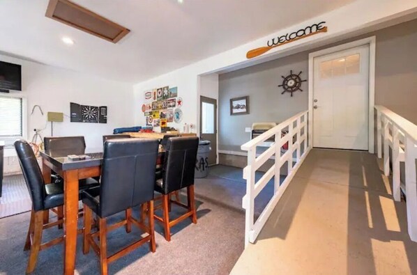 A dining area with a wooden table and chairs, a 'Welcome' sign above the door, and a wall with various decorations. - Escape Reality Docked on Sand Point (Pigeon)