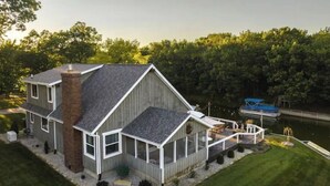 Une maison à deux étages dotée d’une grande terrasse et d’un quai s’avançant dans un lac.