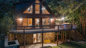 Eine Blockhütte mit Balkon, Steinunterbau und einer Treppe, die zu einer oberen Ebene führt.