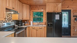 Eine Küche mit Holzausstattung, einem Edelstahlherd, einem Kühlschrank und einem Fenster mit Blick auf Bäume.
