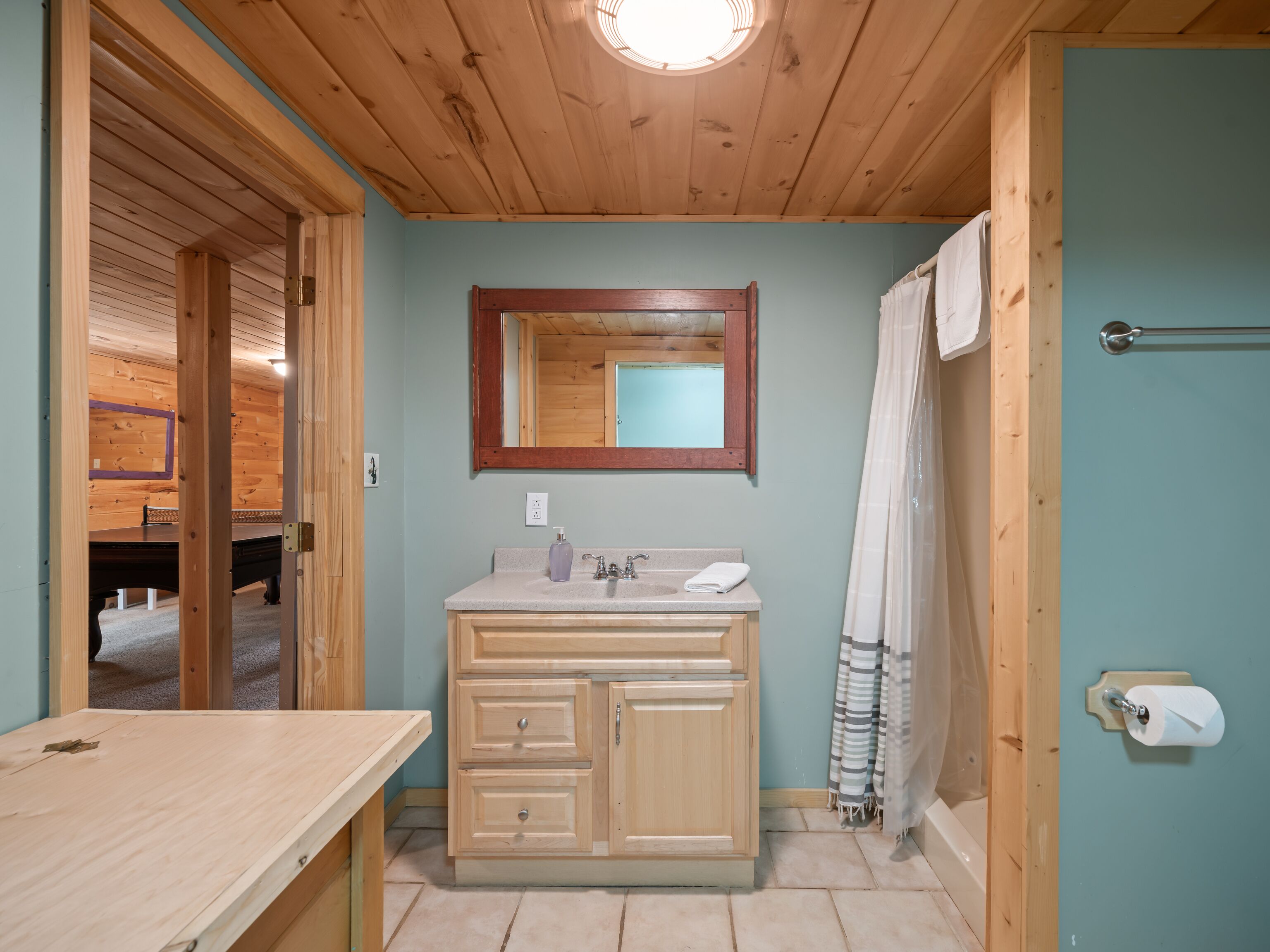 A wooden cabin bathroom with a wooden vanity, a mirror, a sink, and a shower curtain.