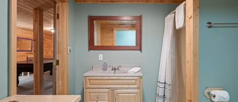 A wooden cabin bathroom with a wooden vanity, a mirror, a sink, and a shower curtain.