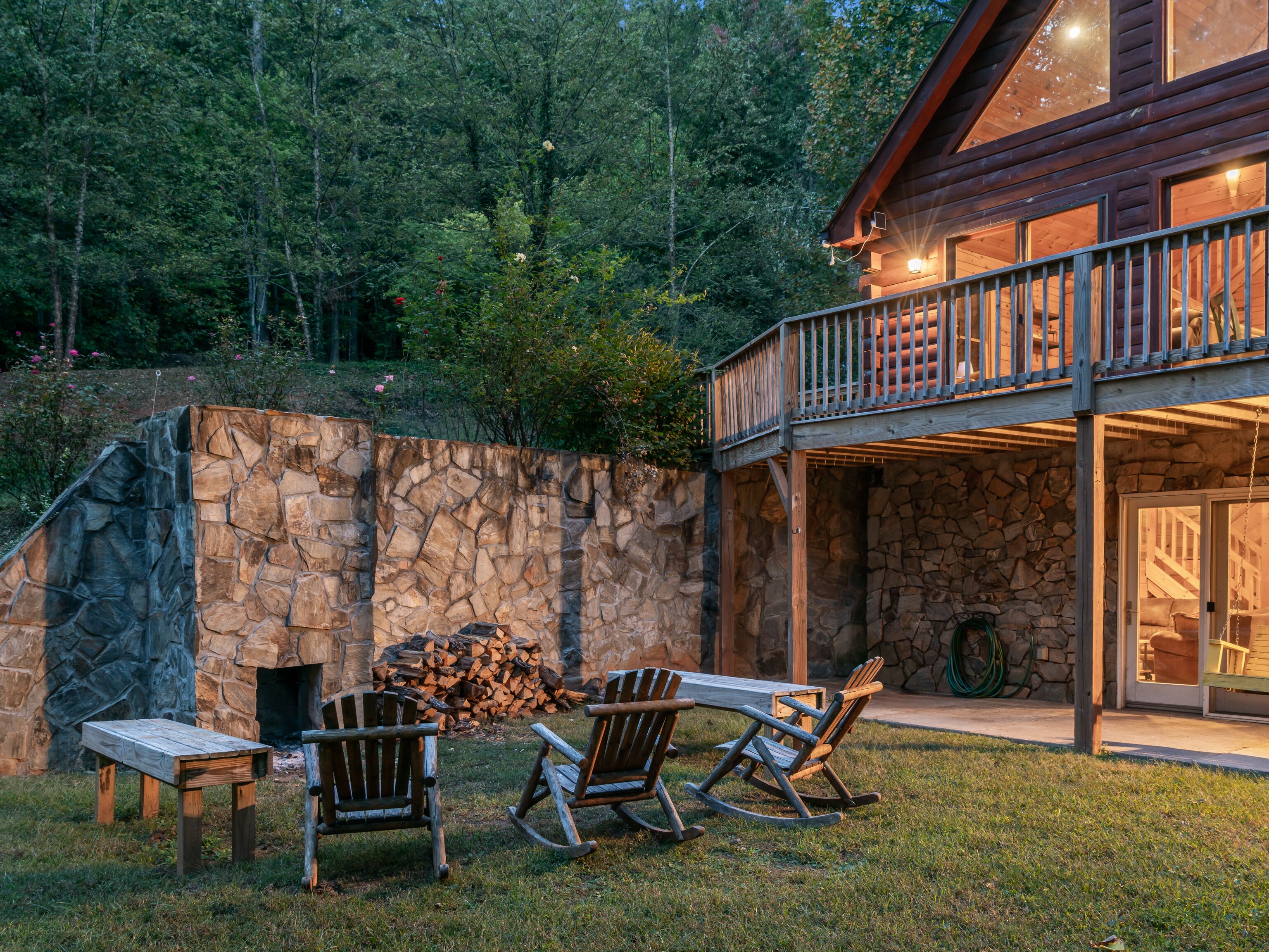 A cabin with a stone wall, a wooden deck, and outdoor seating.