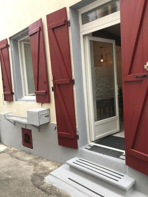 A building with red shutters, a white door, and a small outdoor seating area with a bench. - A Cozy Home (Nérac)