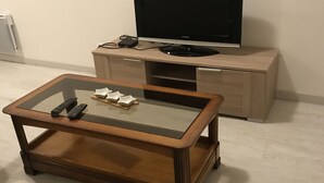 Een woonkamer met een salontafel met glazen blad, een televisie op een houten kast en een bank.